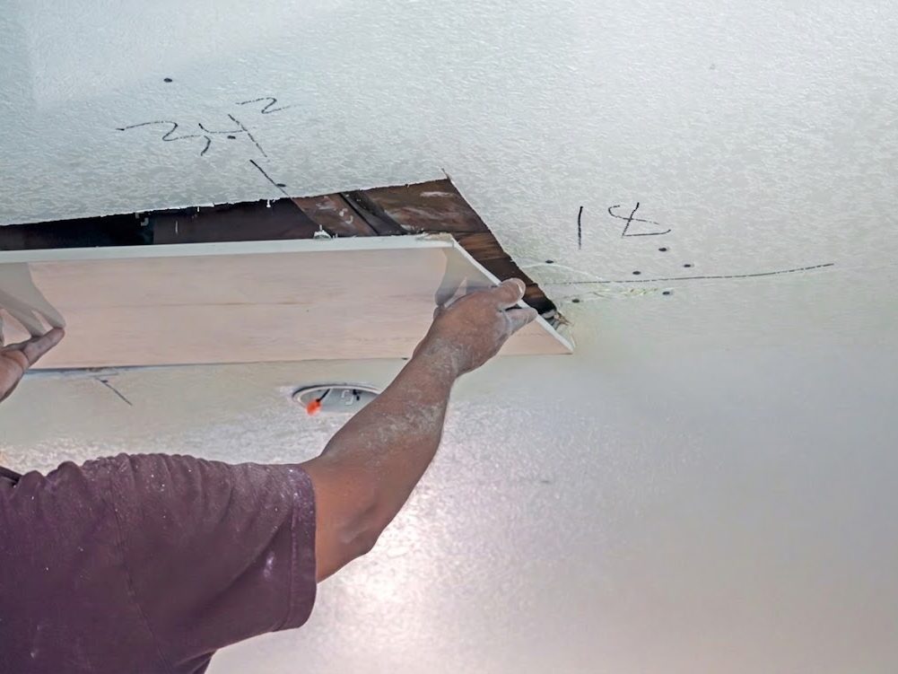 Replacement ceiling board being fitted into a cut opening in a damaged ceiling