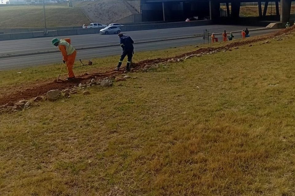 Two operatives trimming and levelling a roadside verge alongside a carriageway